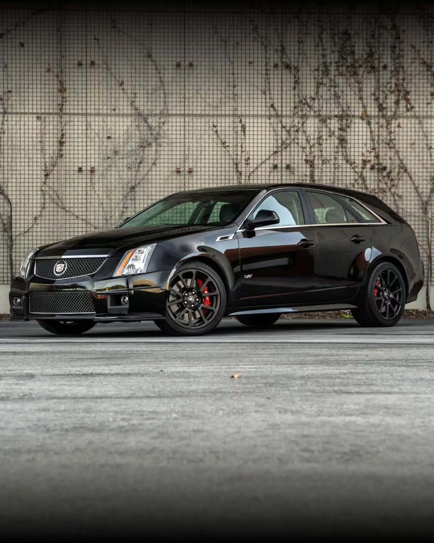 تصویری از نمای خارجی خودروی نادر و عملکردی کادیلاک CTS-V اسپورت واگن (CTS-V Sport Wagon) مدل ۲۰۱۱ تا ۲۰۱۴ با رنگ مشکی یا خاکستری، که طراحی استیشن واگن آن با جزئیات تهاجمی مانند چهار اگزوز و گلگیرهای عریض برای موتور ۶.۲ لیتری V8 سوپرشارژ ۵۶۴ اسب‌بخاری را نشان می‌دهد.