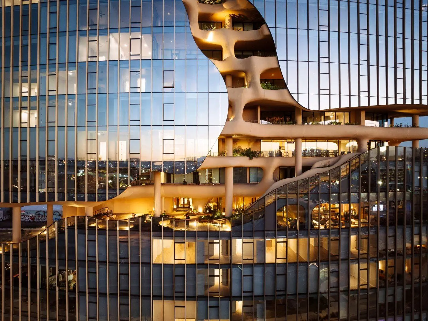 نمای ساختمان وان ریور نورث در دنور با نمای شیشه‌ای و شکاف عمیق صخره‌ای مجهز به گیاهان طبیعی و مسیر پیاده‌روی عمودی.