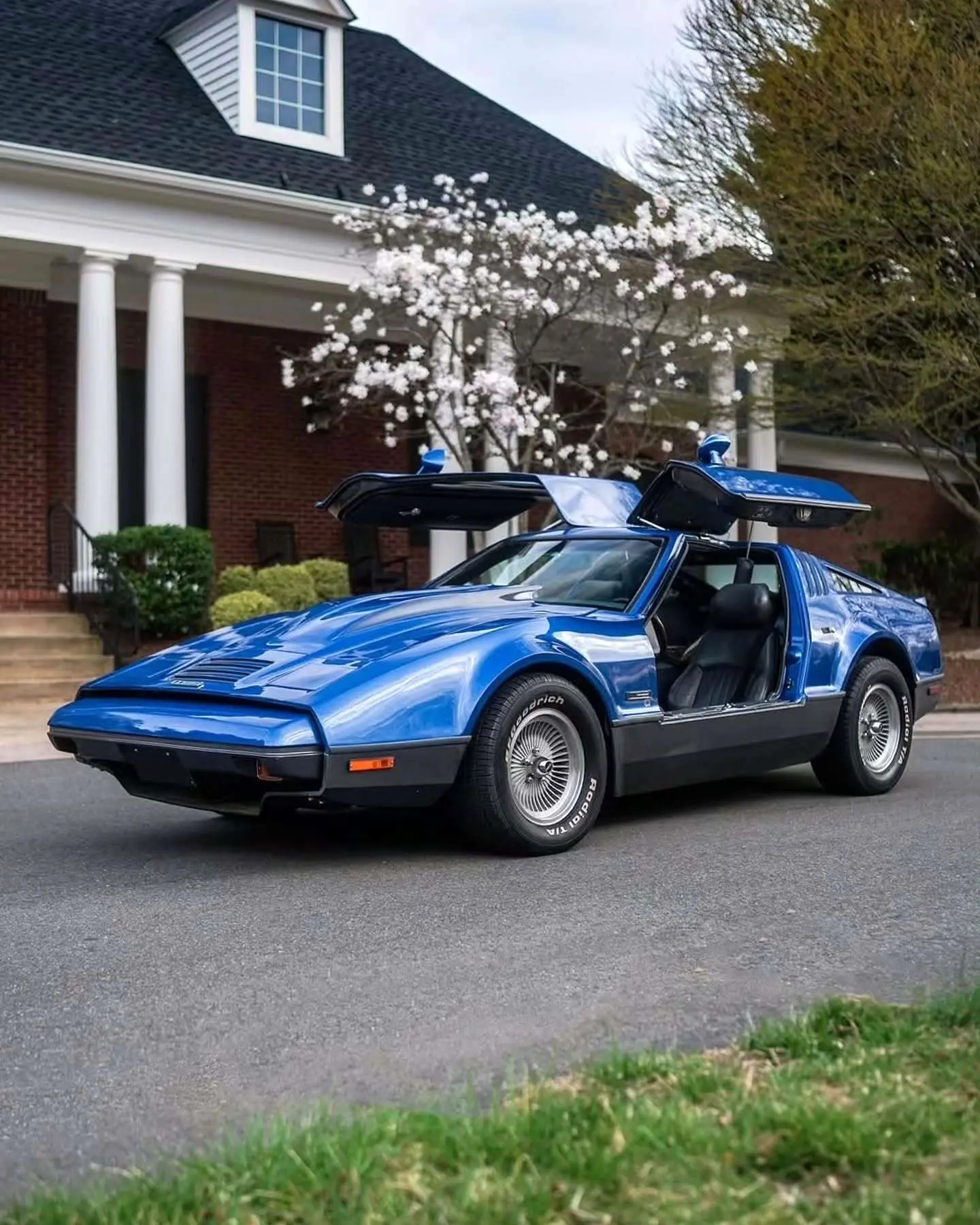 نمای جانبی خودروی کلاسیک بریکلین SV-1 با درهای باز شده رو به بالا و بدنه آکریلیک نارنجی رنگ که طراحی ایمن و آیرودینامیک آن را نشان می‌دهد.