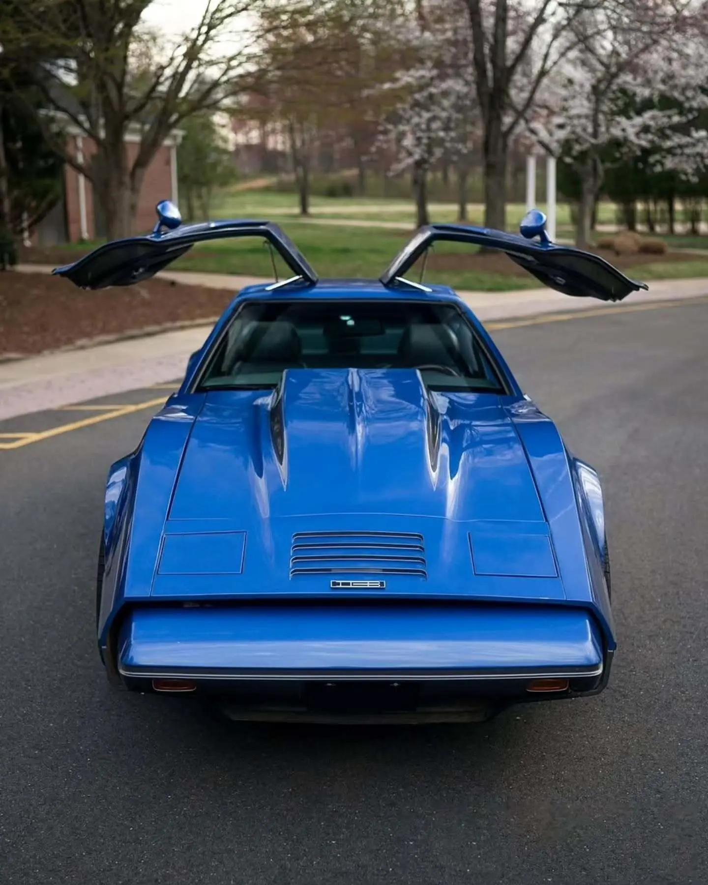 نمای جانبی خودروی کلاسیک بریکلین SV-1 با درهای باز شده رو به بالا و بدنه آکریلیک نارنجی رنگ که طراحی ایمن و آیرودینامیک آن را نشان می‌دهد.