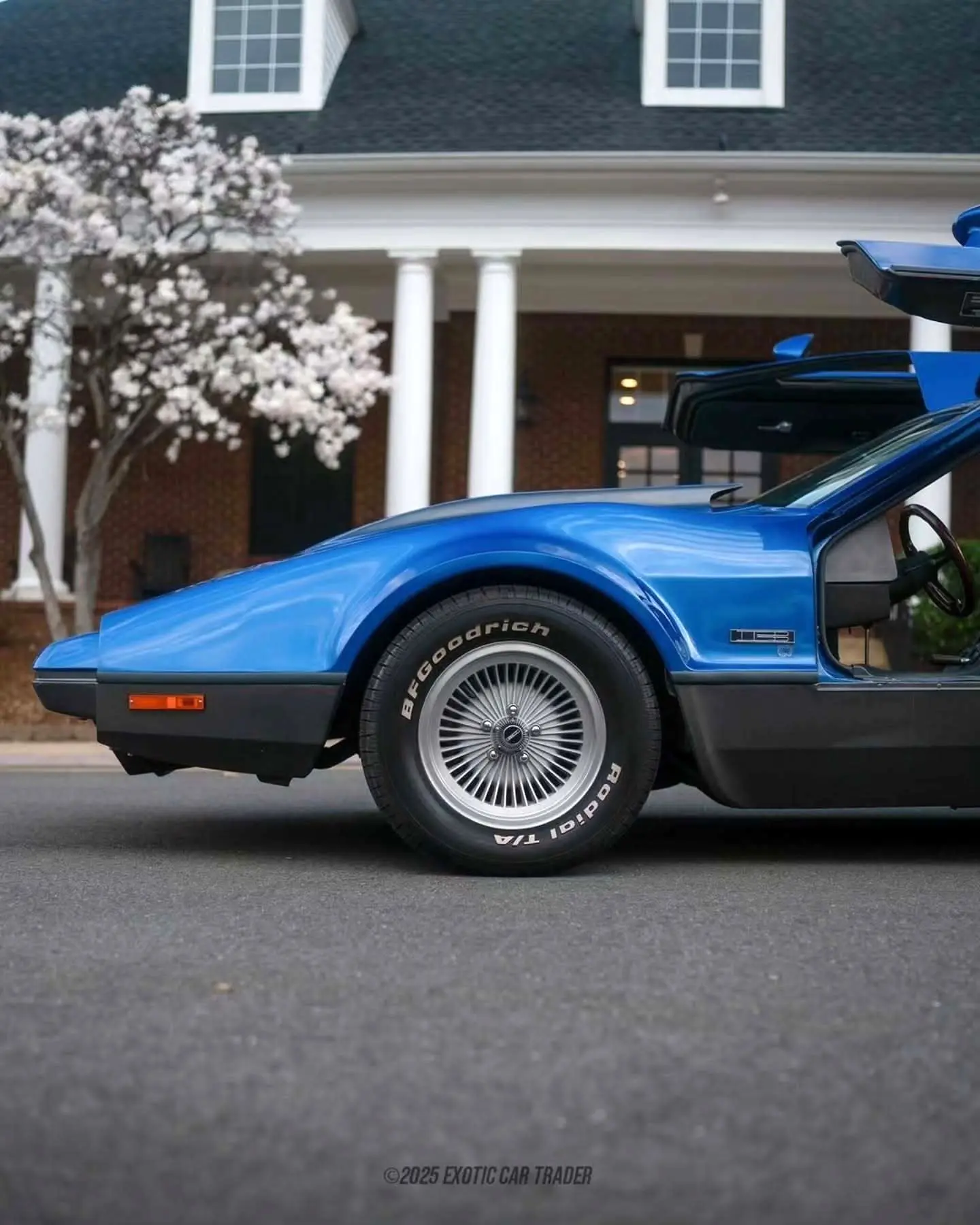 نمای جانبی خودروی کلاسیک بریکلین SV-1 با درهای باز شده رو به بالا و بدنه آکریلیک نارنجی رنگ که طراحی ایمن و آیرودینامیک آن را نشان می‌دهد.