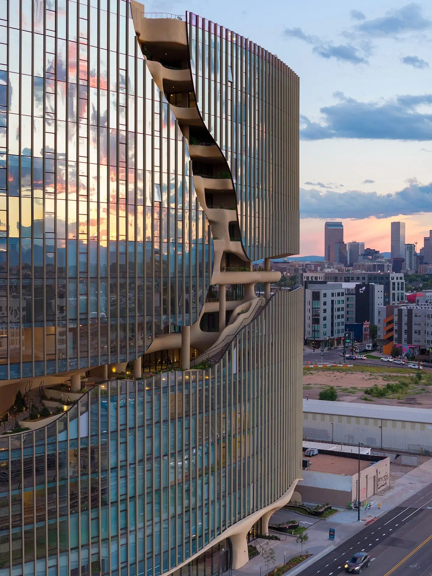 نمای ساختمان وان ریور نورث در دنور با نمای شیشه‌ای و شکاف عمیق صخره‌ای مجهز به گیاهان طبیعی و مسیر پیاده‌روی عمودی.